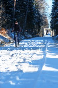 Ryd, Sweden - February 16, 2016: An old iron railway bridge now used as a walk and cycle path through the forest. It is winter and some snow is on the ground. Unknown person cycle on the path.